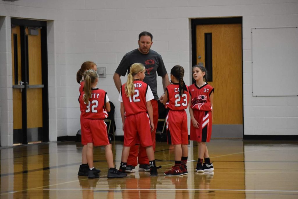 Youth basketball coach talking with players in red custom uniforms during a game break